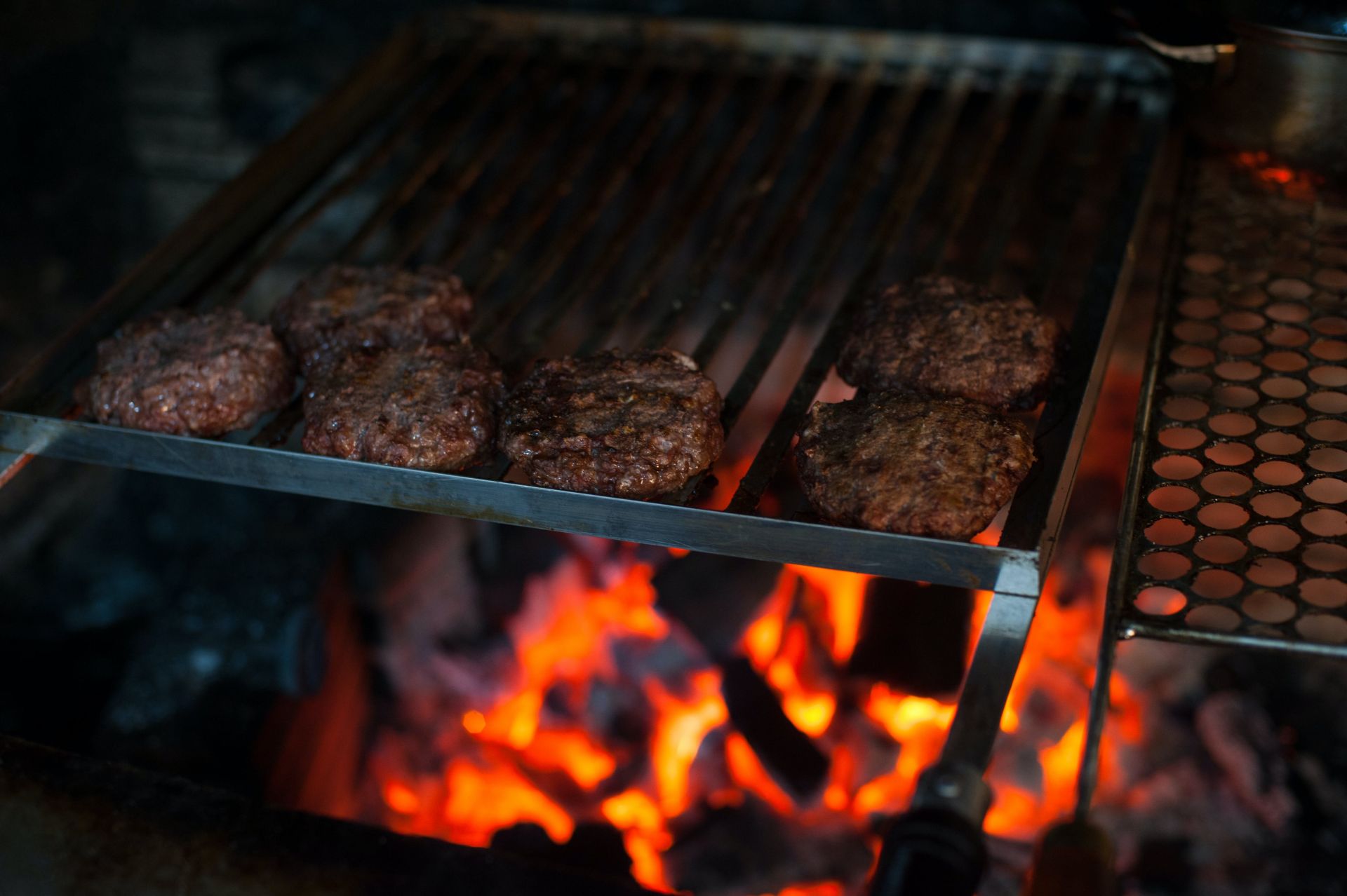 From above of appetizing meat patties grilling on metal barbecue grade above fire in kitchen